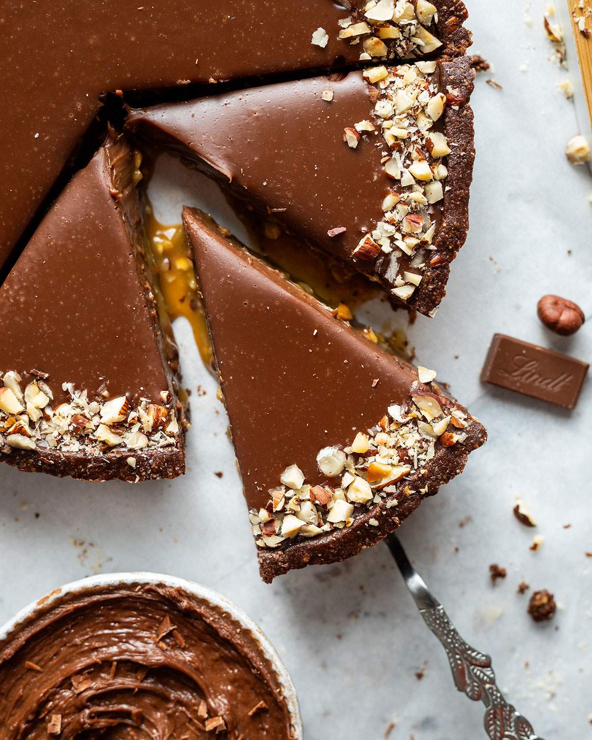 Sliced vegan chocolate tart from above with one slice pulled from the tart, showing the caramel sauce.
