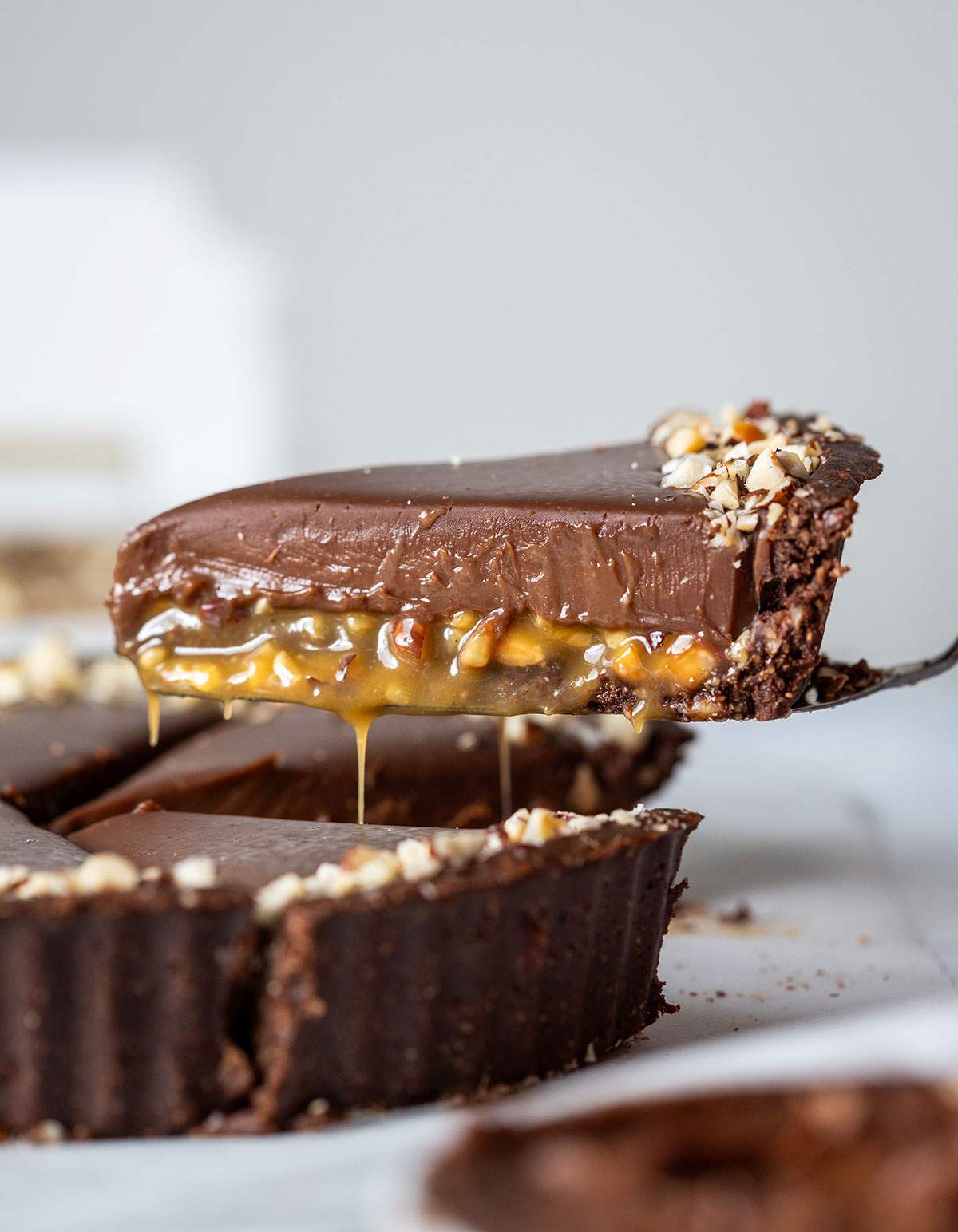 A cake lifter picking up a slice of chocolate tart with caramel, clearly showing the layers of nutty caramel and smooth chocolate.