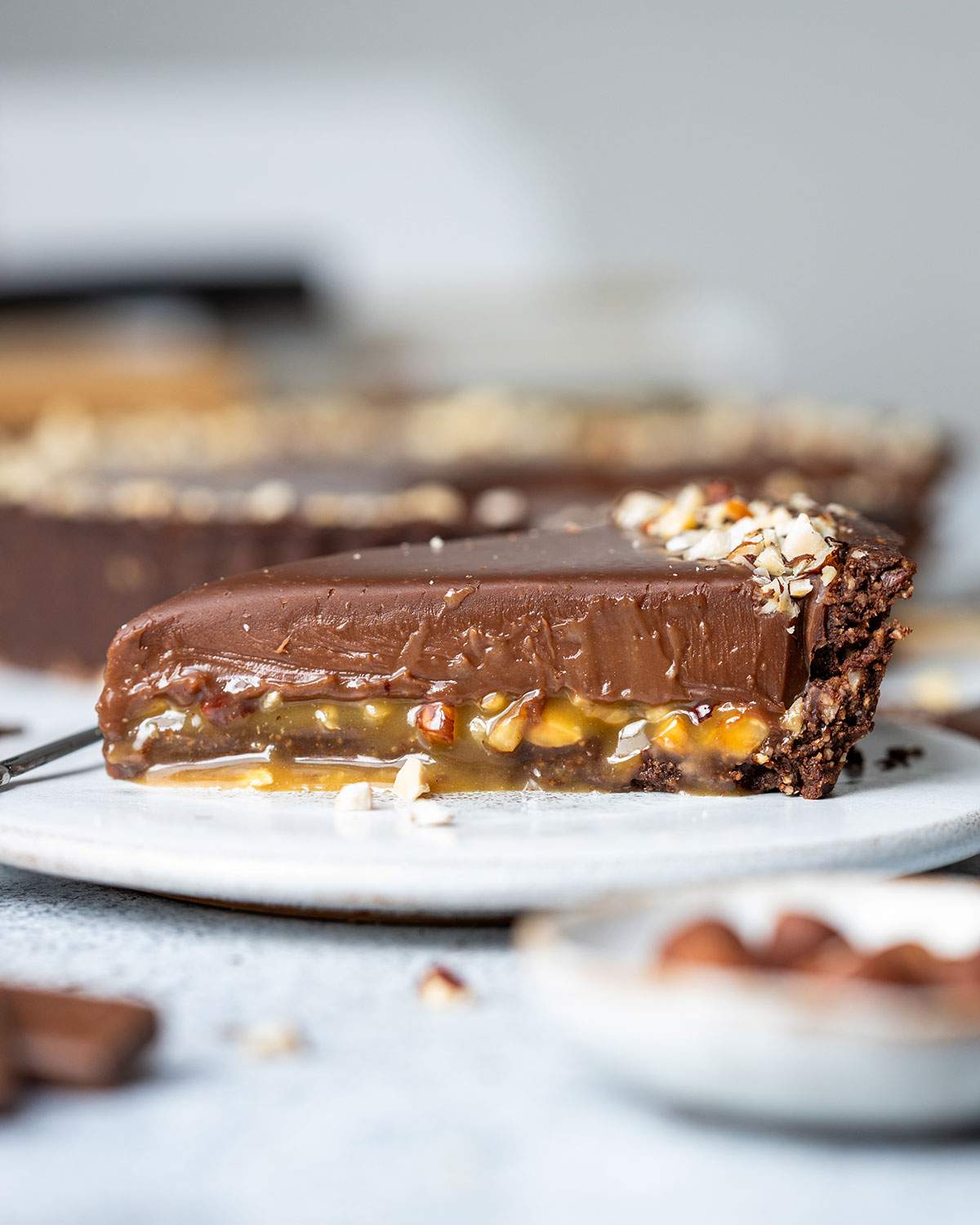 A slice of chocolate caramel tart on a dessert plate, shown from the side with all layers visible.