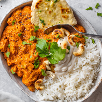 A serving plate with vegan tikka masala alongside basmati rice, fresh cilantro and naan bread on the side.