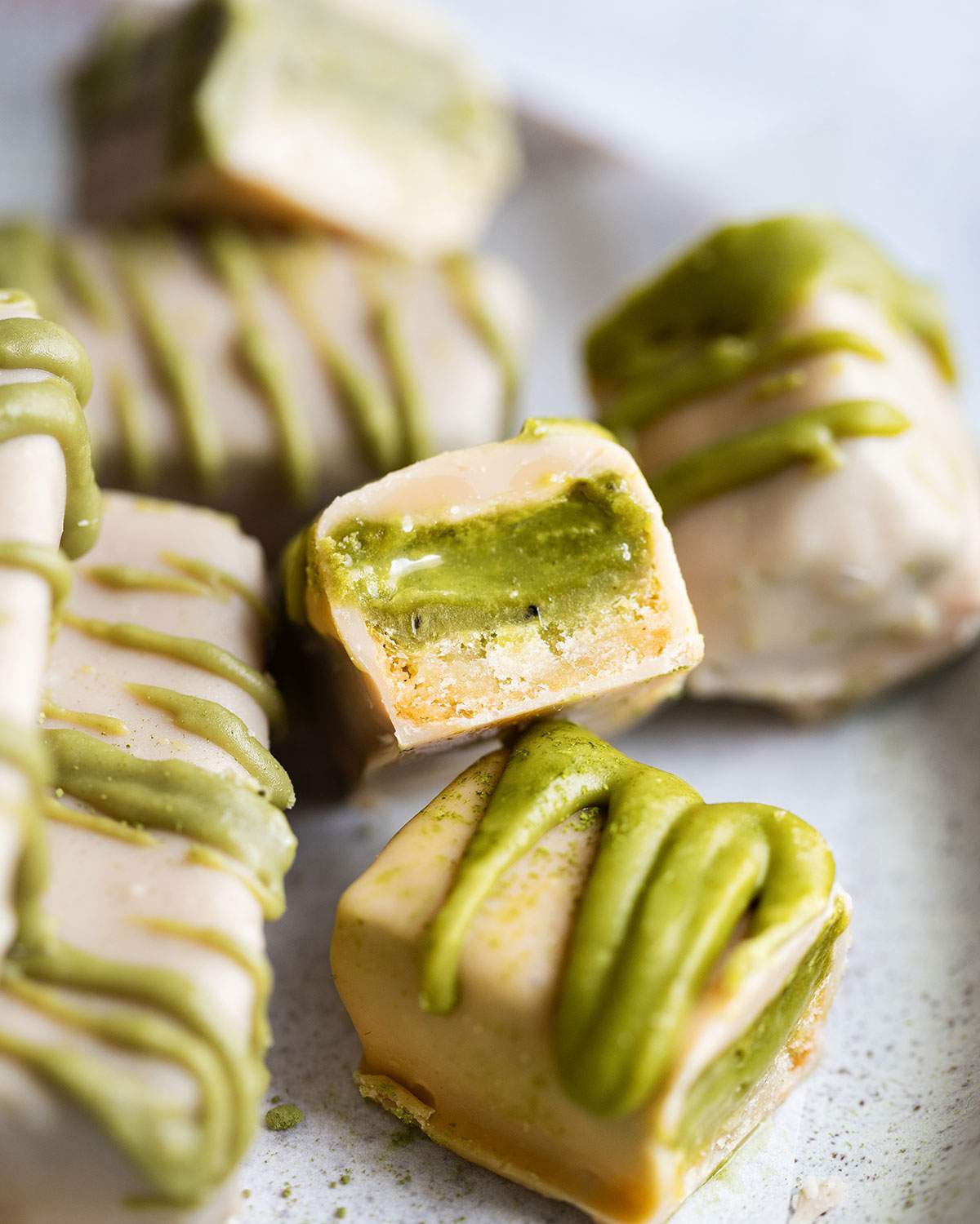 White chocolate matcha twix bars on a serving plate and one bar is cut in half and you can clearly see the green matcha caramel inside the bar.