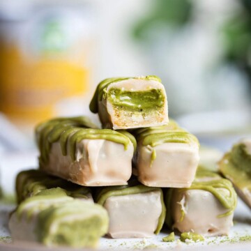 A white chocolate matcha caramel bar is cut in half and placed on top of a stack of chocolate bars.