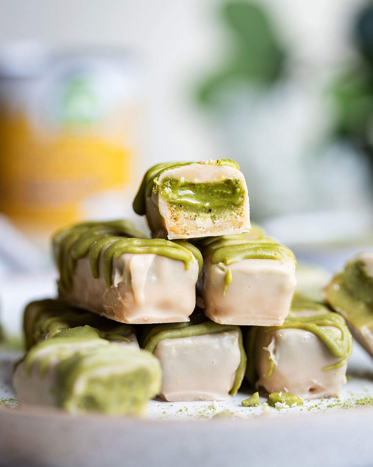 A white chocolate matcha caramel bar is cut in half and placed on top of a stack of chocolate bars.