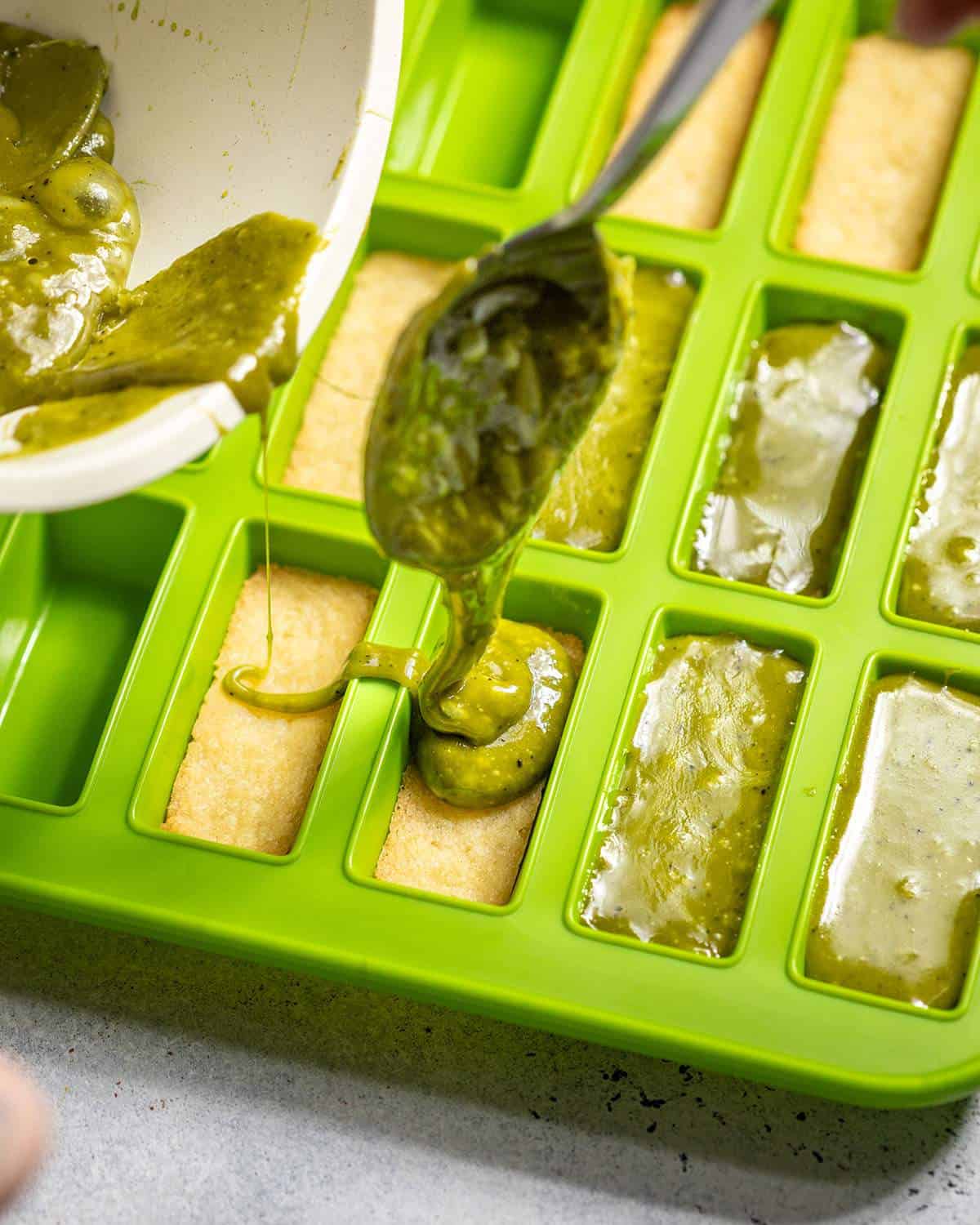 A spoon is transferring homemade matcha caramel into chocolate moulds.