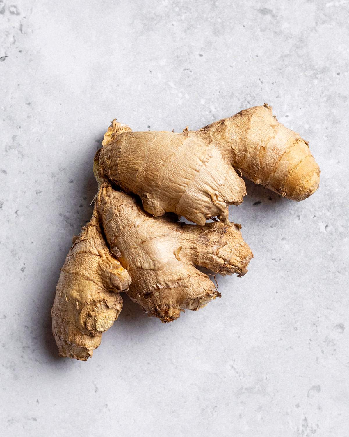 A fresh, wrinkled piece of ginger on a white marble table.