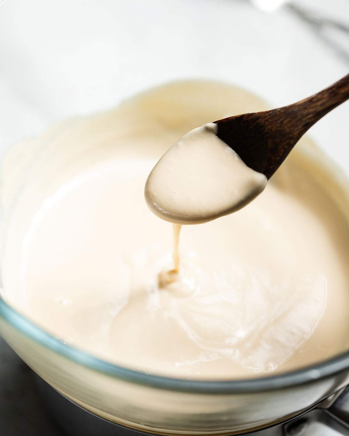 A spoon is lifting melted white chocolate out of a bowl.