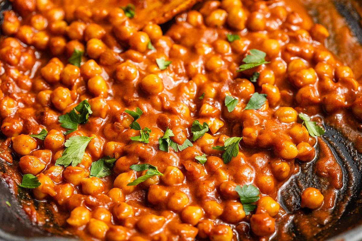 Creamy vegan buffalo chickpeas in a skillet with herbs on top.