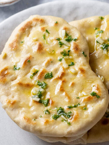 Vegan Garlic Naan bread on a serving plate with fresh cilantro and garlic butter on top.