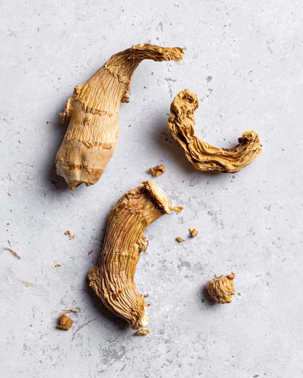 3 large pieces of dried and wrinkly ginger laying on a white table.