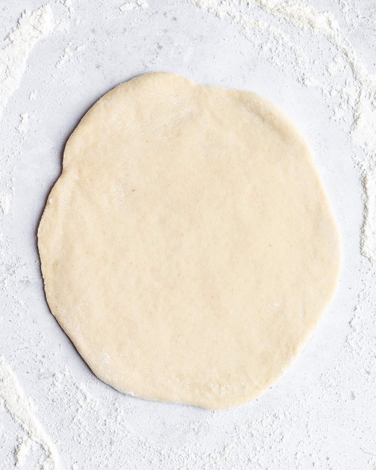 Rolled out flatbread dough on a smooth surface.