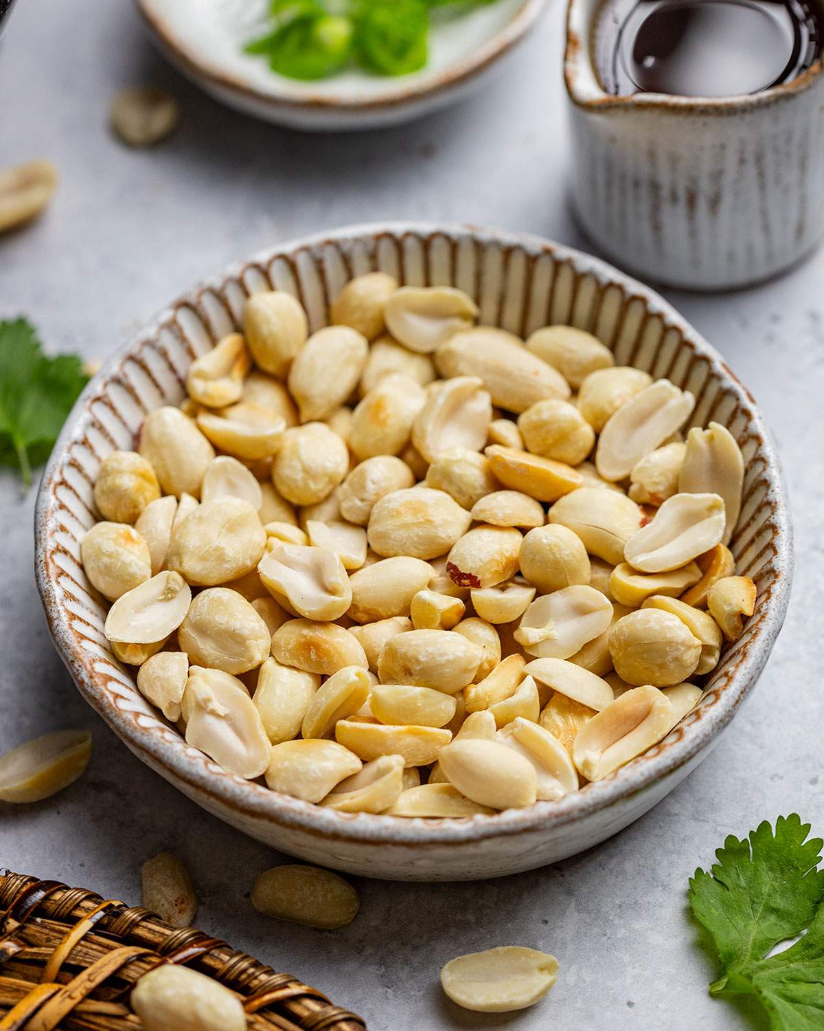 A bowl of peanuts next to other pad thai ingredients on the table.