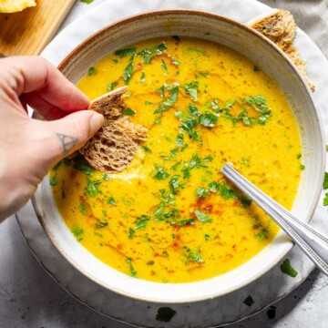 A vibrant bowl of lemon soup and a piece of bread dipped into it.