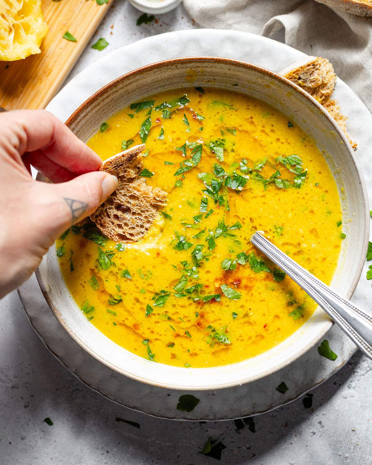 A vibrant bowl of lemon soup and a piece of bread dipped into it.