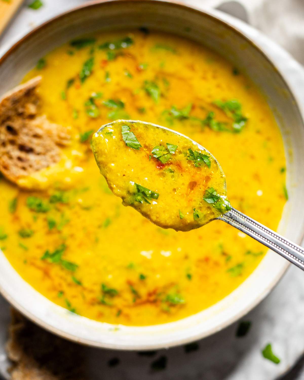 A spoonful of lemon soup above a soup bowl.