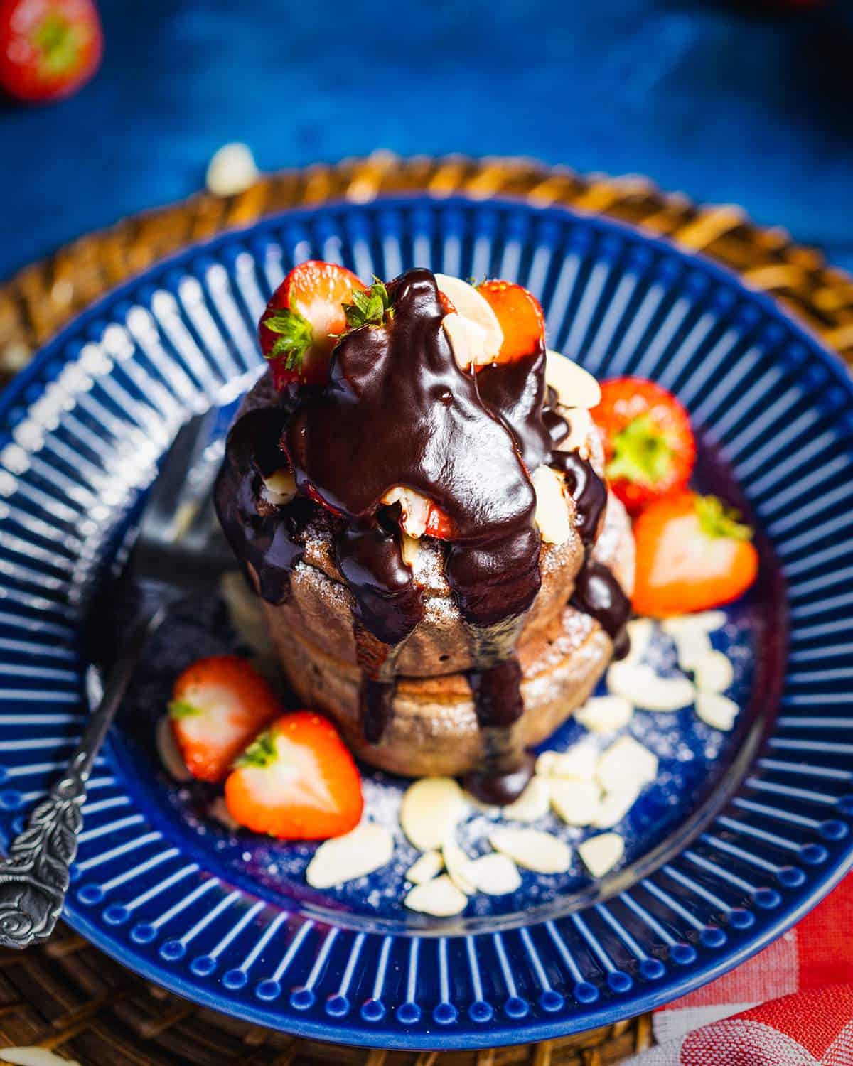 Stacked vegan soufflé pancakes with strawberries and chocolate sauce on a blue plate.