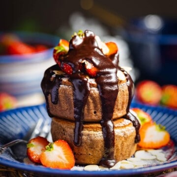 Two vegan soufflé pancakes with strawberries and chocolate sauce on top.