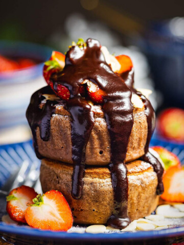 Two vegan soufflé pancakes with strawberries and chocolate sauce on top.