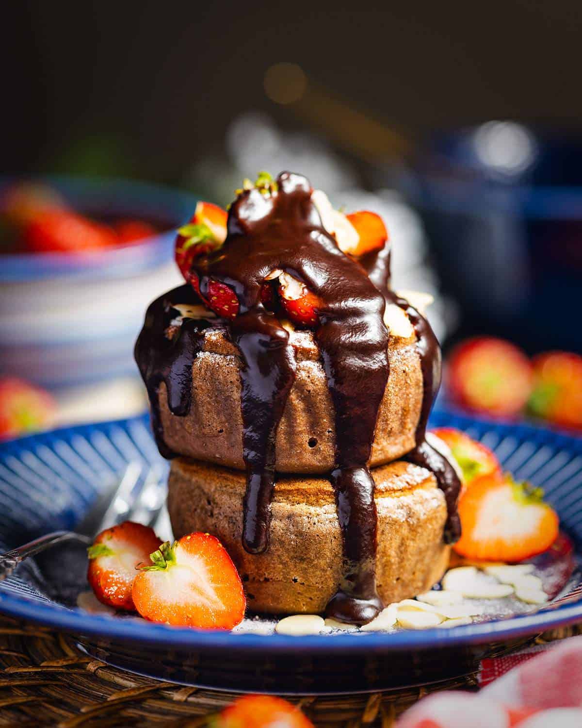 Two vegan soufflé pancakes with strawberries and chocolate sauce on top.