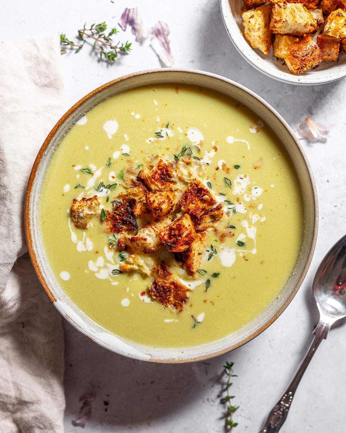 A bowl of creamy, vegan asparagus soup topped with homemade croutons and fresh thyme.