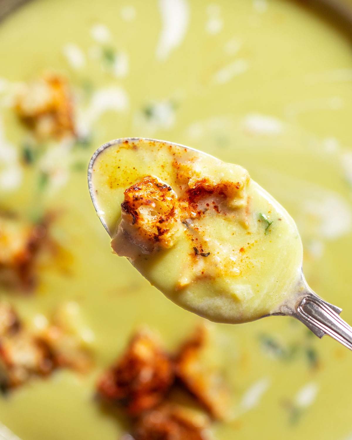 A spoon lifting asparagus soup from a soup bowl.