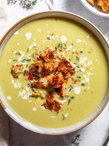 A bowl of vegan green asparagus soup with croutons and fresh thyme.