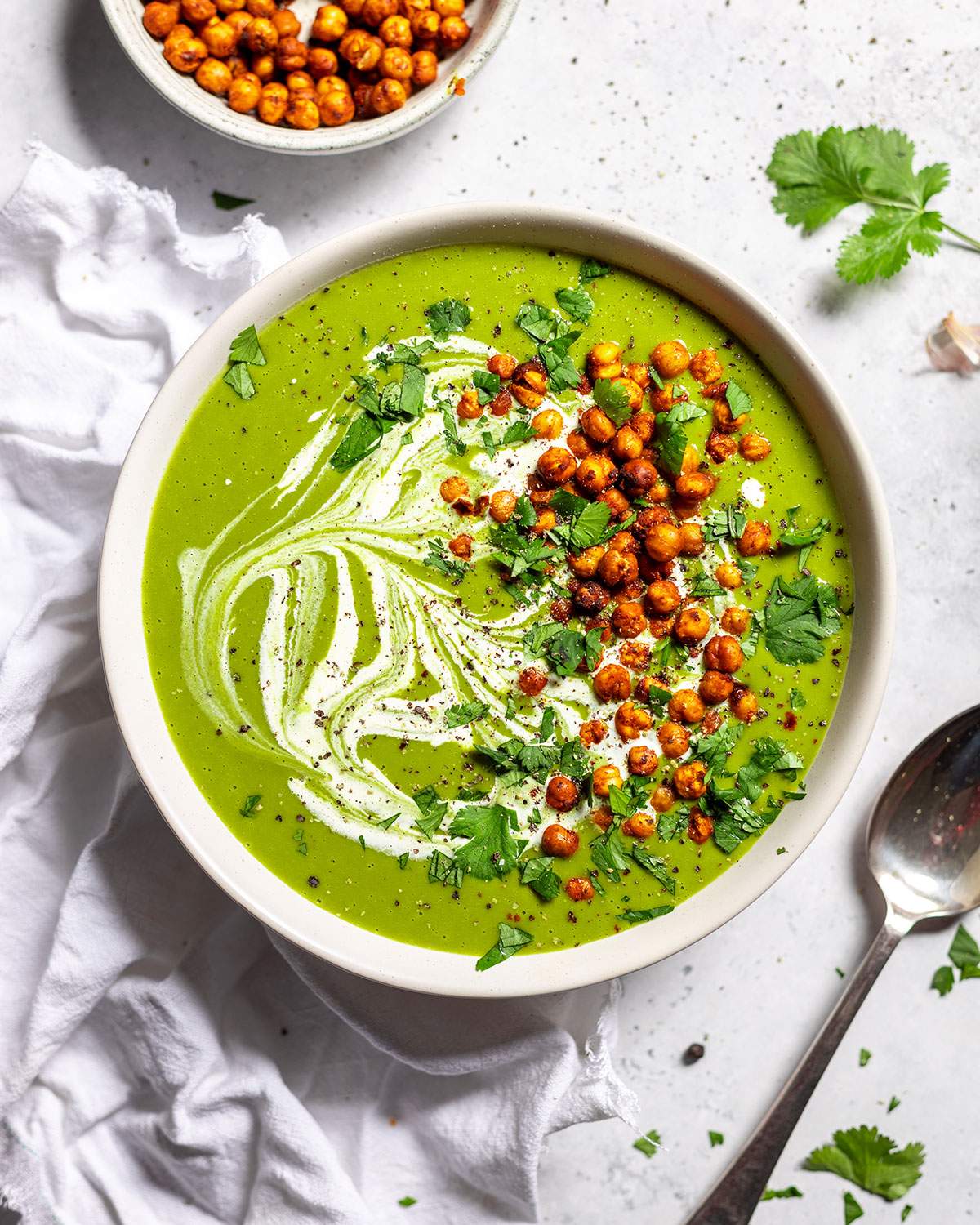 A bowl filled with creamy pea and kale soup, topped with crunchy baked chickpeas and fresh parsley.