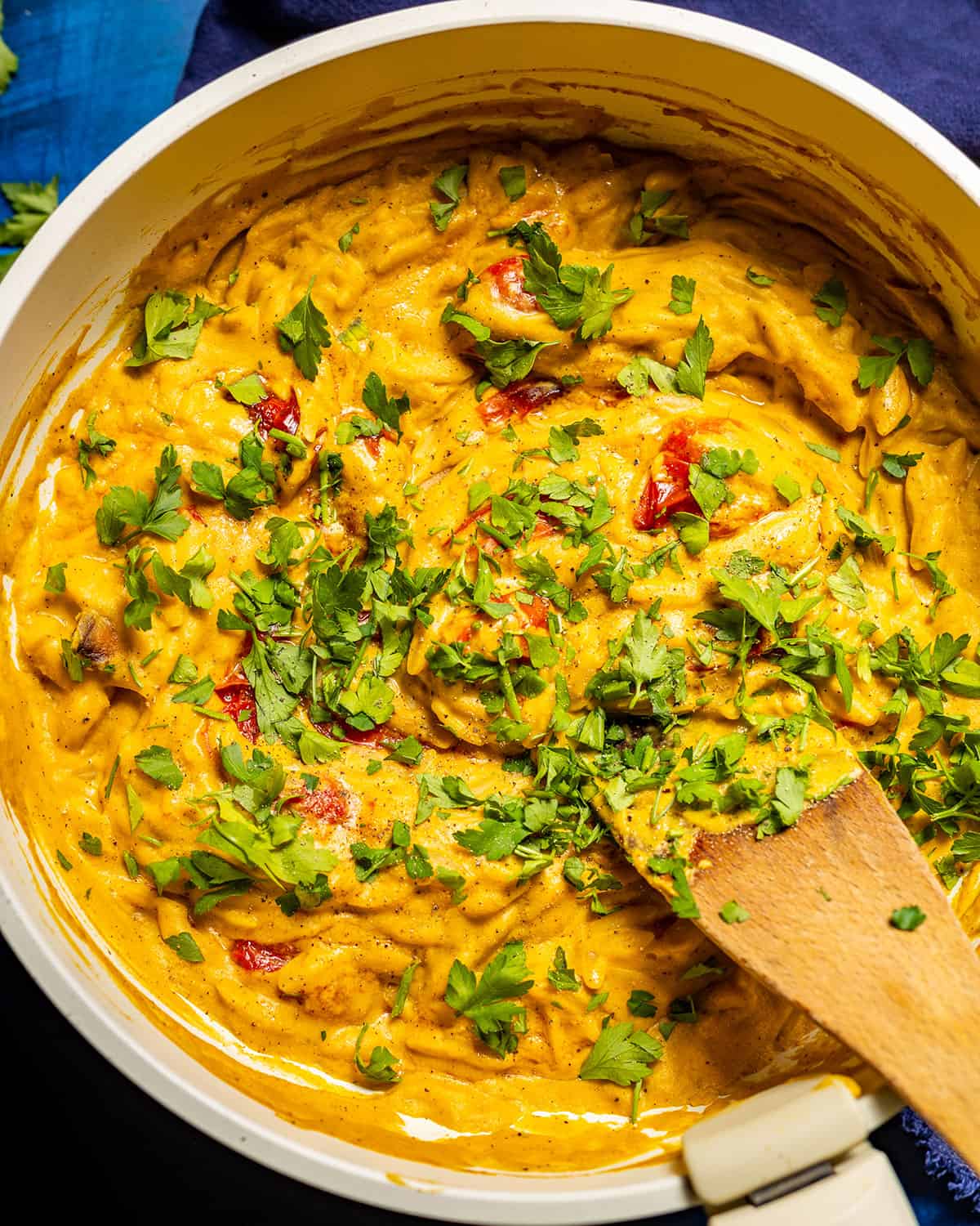 A skillet filled with vibrant butternut squash orzo topped with fresh herbs.