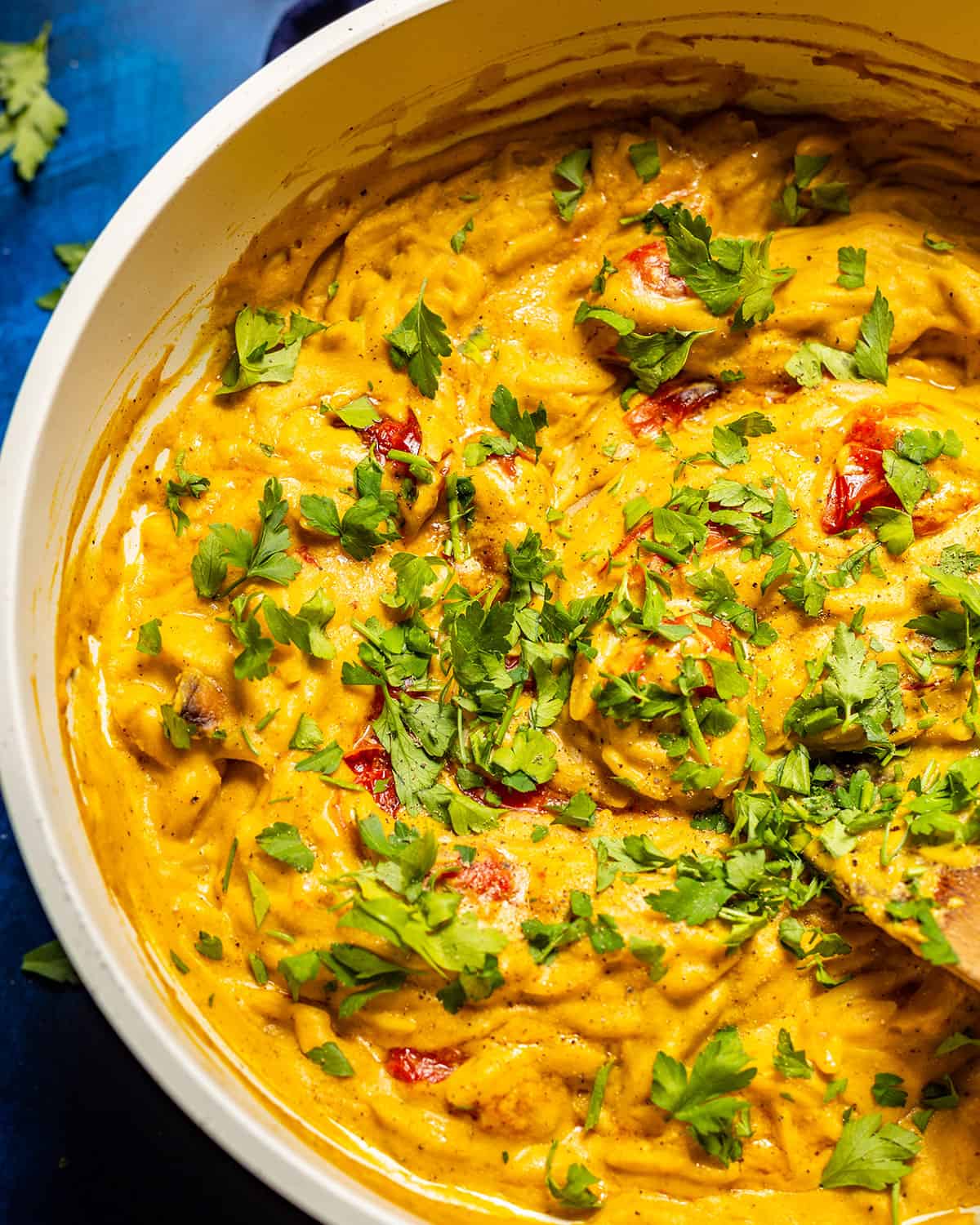 A skillet filled with vibrant butternut squash orzo topped with fresh herbs.