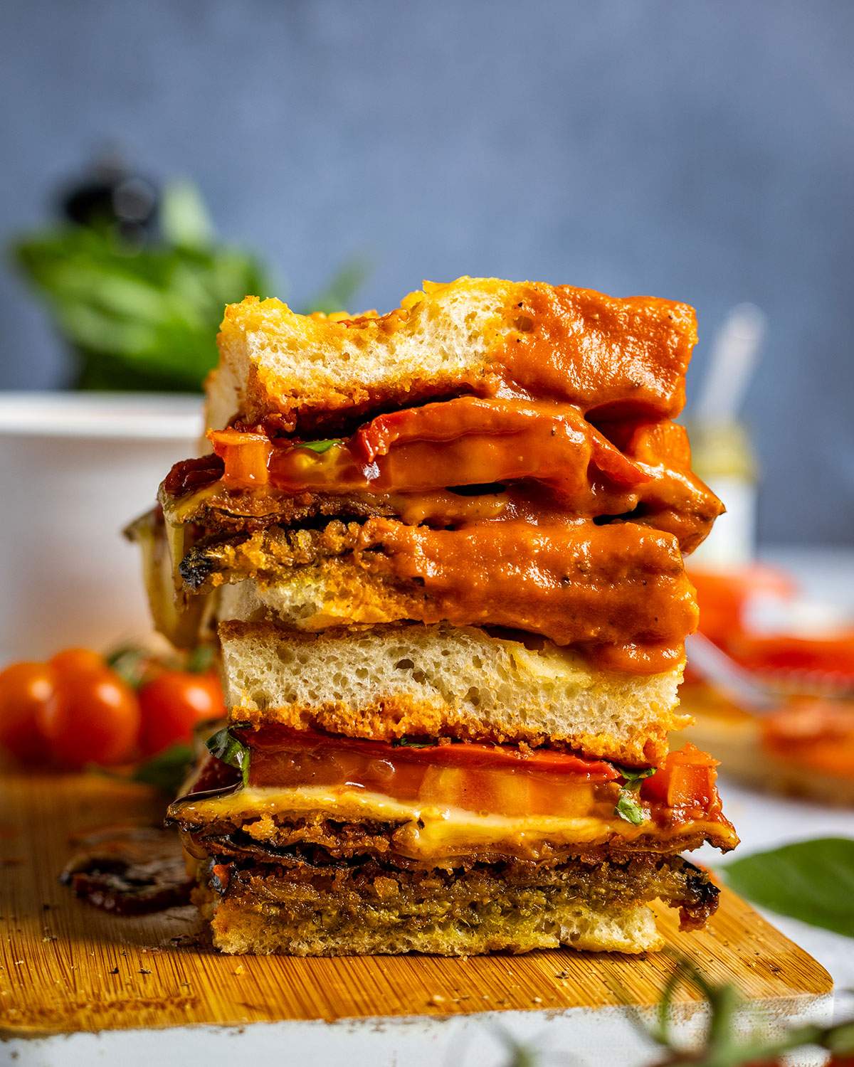 Two slices of a vegan focaccia sandwich stacked on top of each other. The top half has been dipped into tomato soup.