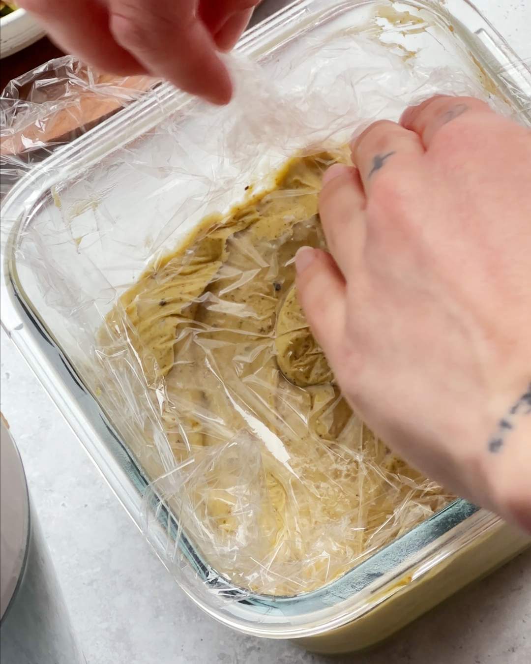 Covering ice cream in a glass container with plastic wrap.