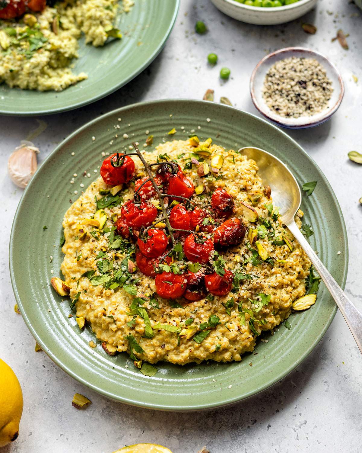 Creamy quinotto aka quinoa risotto served on a green plate with fresh herbs and roasted cherry tomatoes on top.