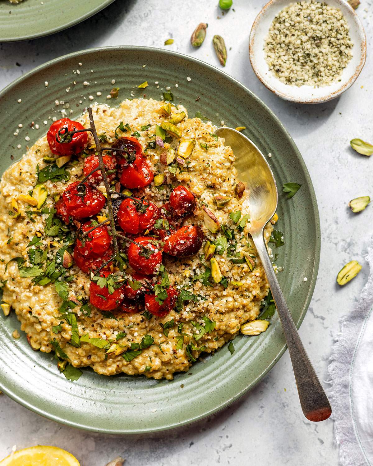 Creamy quinotto aka quinoa risotto served on a green plate with fresh herbs and roasted cherry tomatoes.