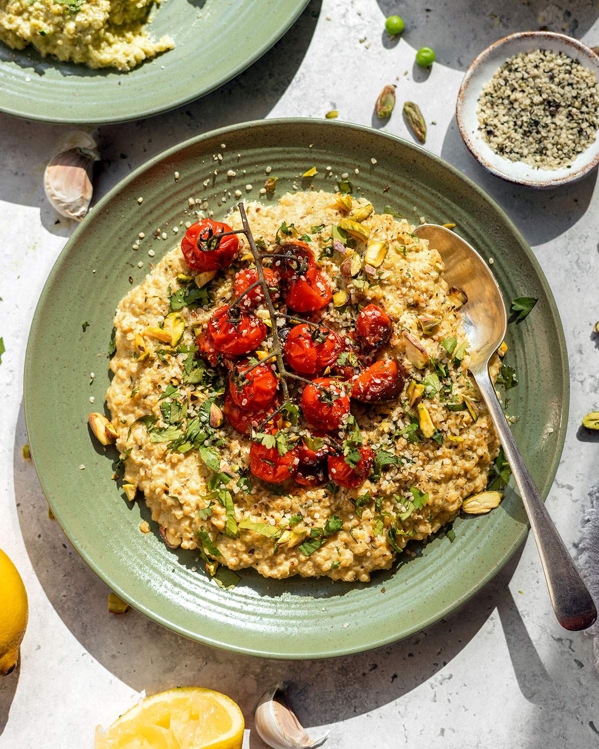 Creamy quinotto on a green plate with fresh herbs and roasted cherry tomatoes on top.