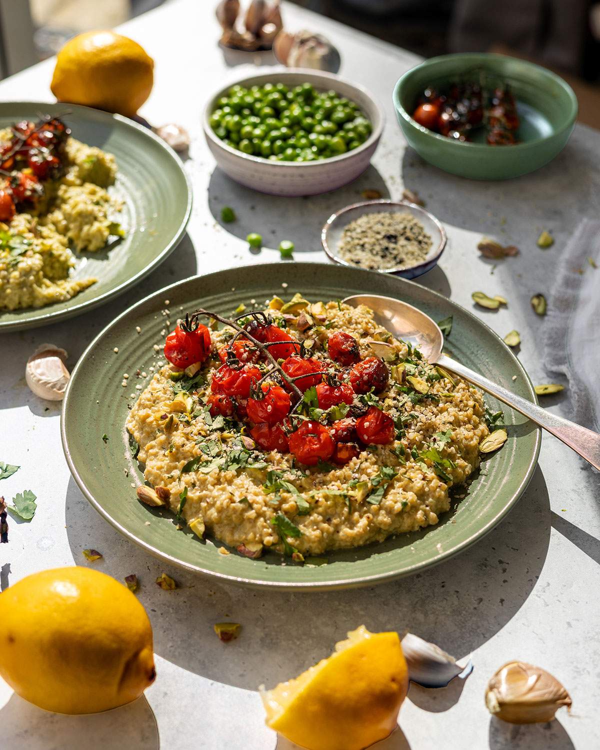 Creamy vegan quinoa risotto on a table with fresh herbs and roasted cherry tomatoes.