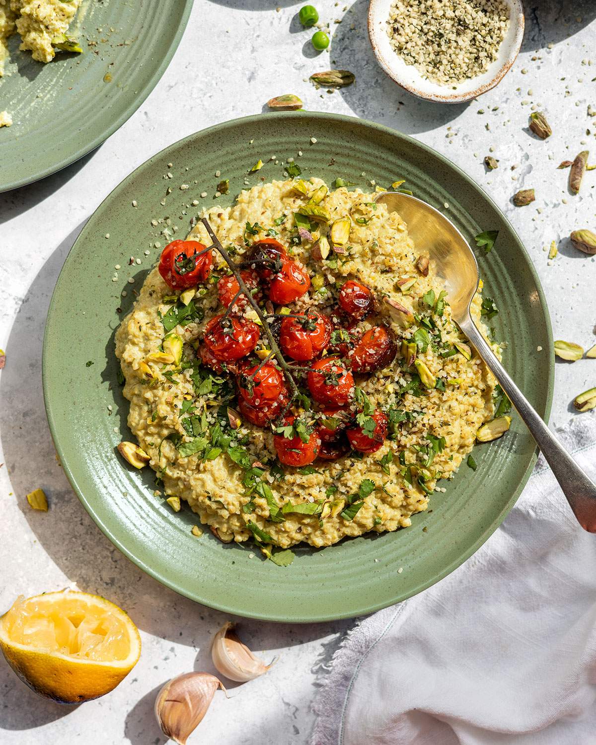 Creamy quinotto aka quinoa risotto served on a green plate with fresh herbs and roasted cherry tomatoes on top.