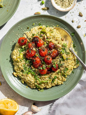 Creamy quinotto aka quinoa risotto served on a green plate with fresh herbs and roasted cherry tomatoes on top.