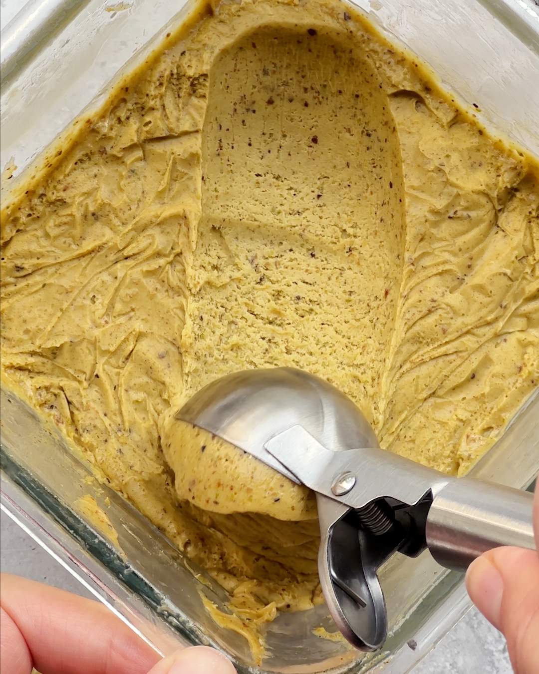 Scooping vegan pistachio ice cream from a freezer container.