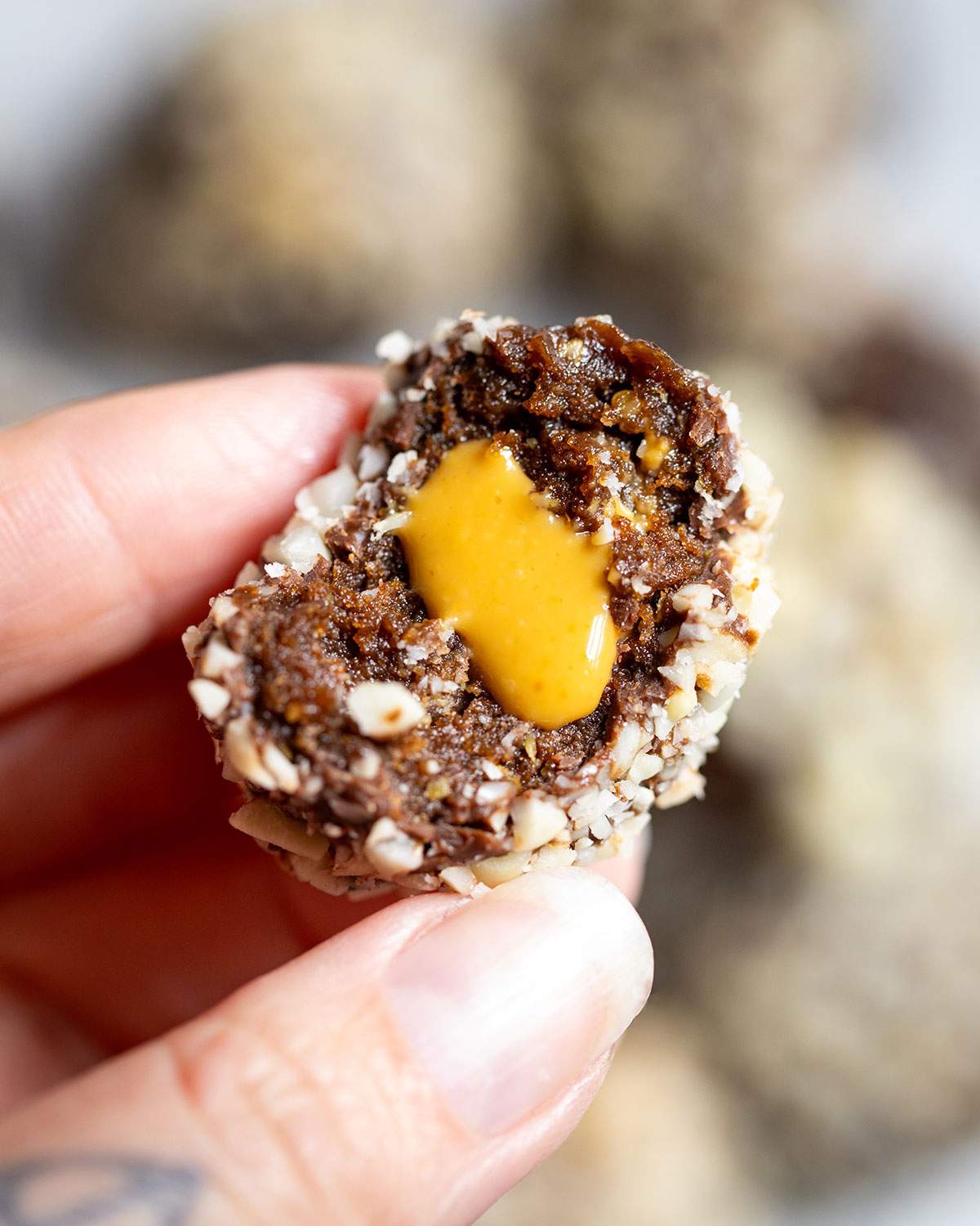 A hand holding a vegan chocolate protein ball with smooth peanut butter oozing from the center.