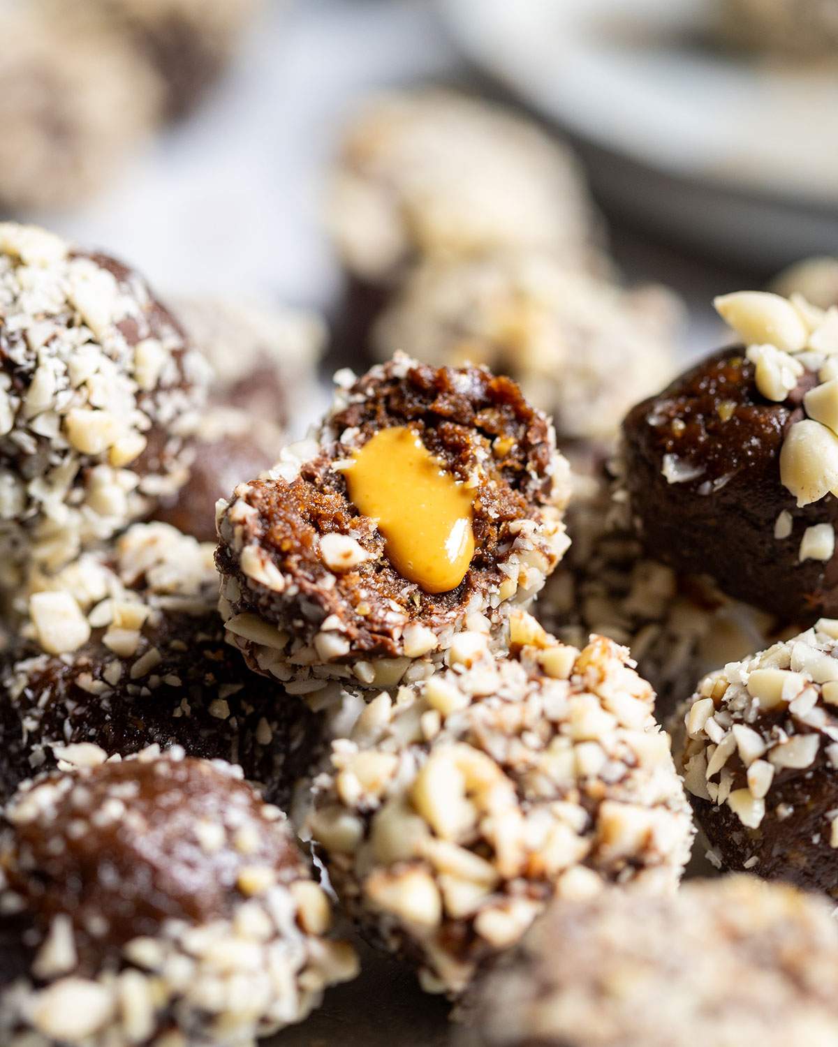 A stack of vegan protein balls with a half eaten snack ball on top, oozing smooth peanut butter from its center.