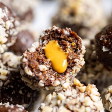 Half a vegan snickers protein ball with a smooth peanut butter filling oozing from the centre, placed on a stack of protein balls.