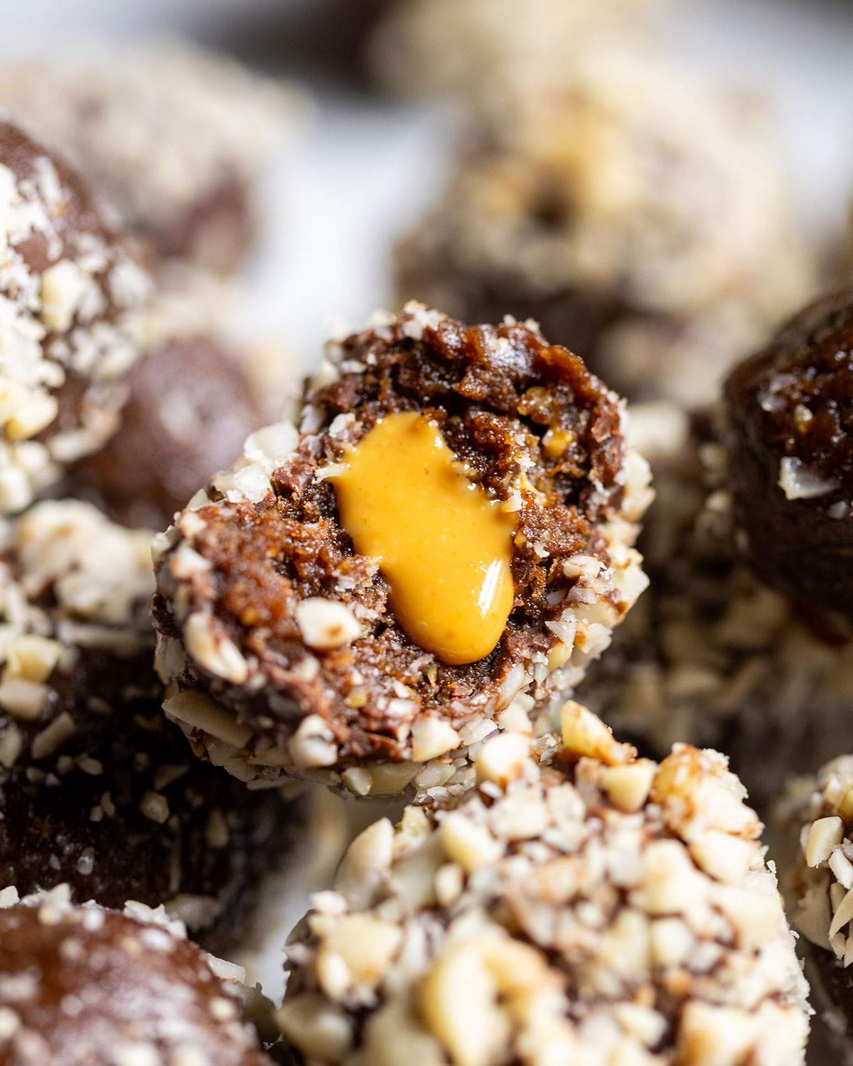 Half a vegan snickers protein ball with a smooth peanut butter filling oozing from the centre, placed on a stack of protein balls.