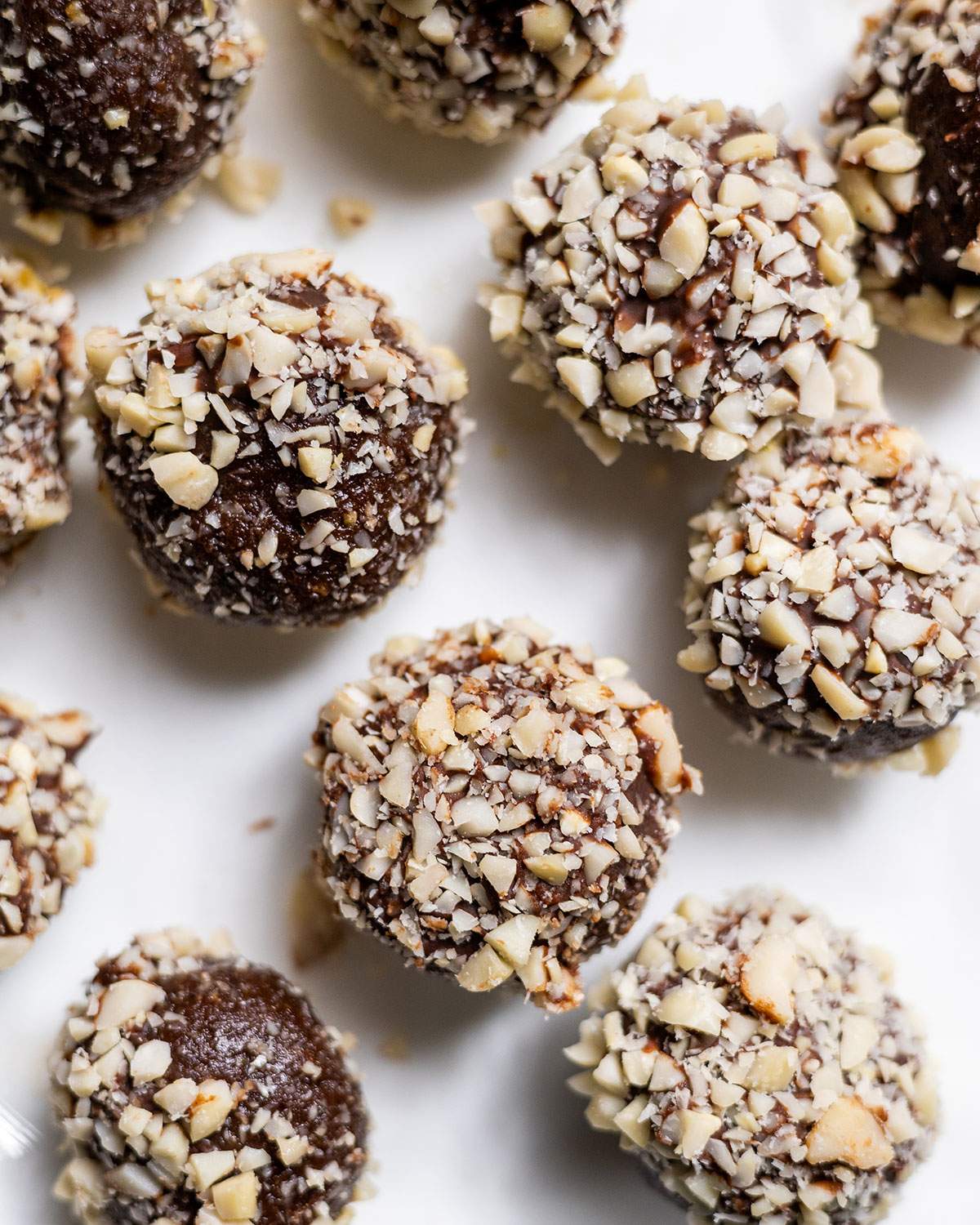 Chocolate flavoured protein snack balls covered in crunchy peanuts on parchment paper.