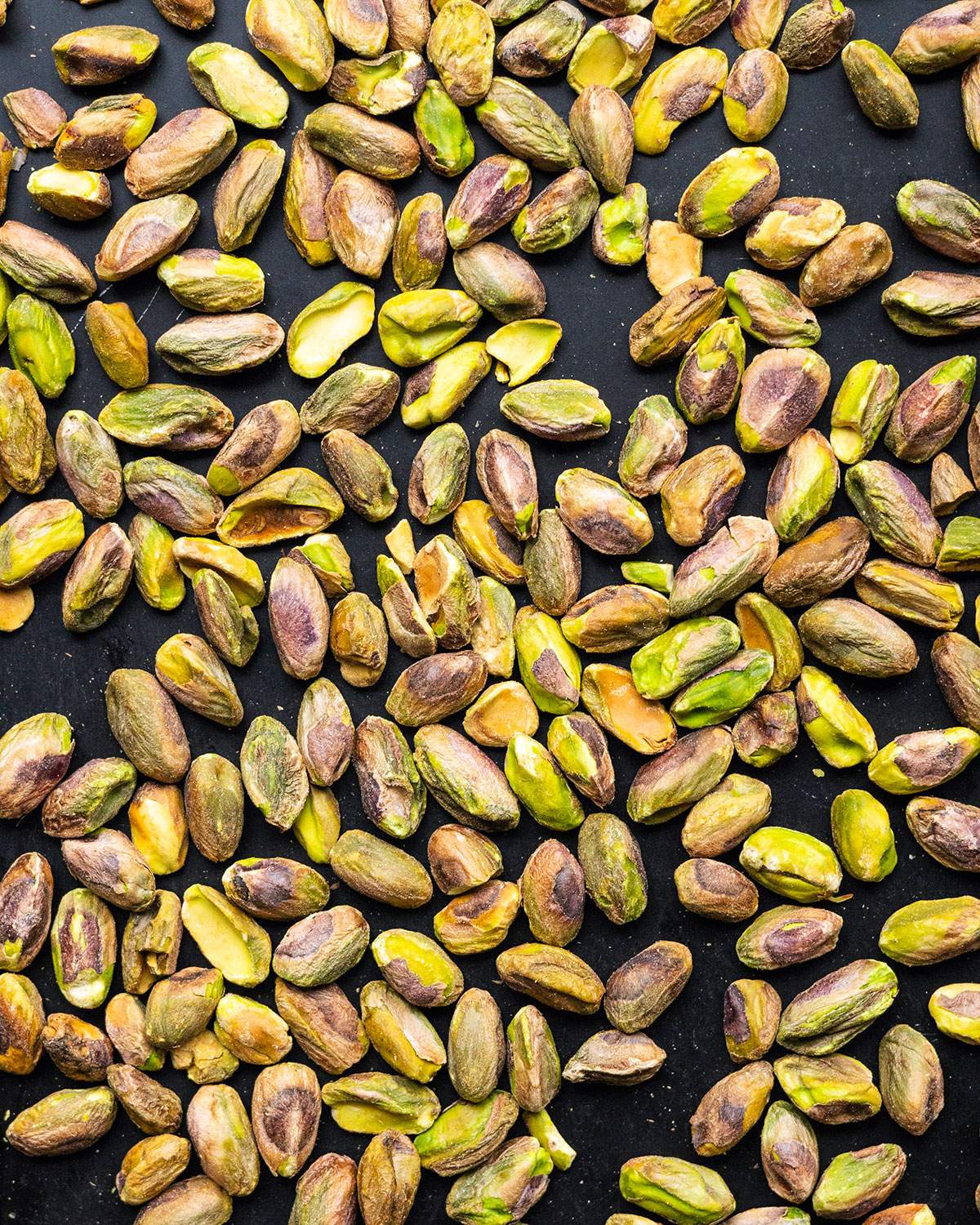 Roasted pistachios up close on a roasting tray.