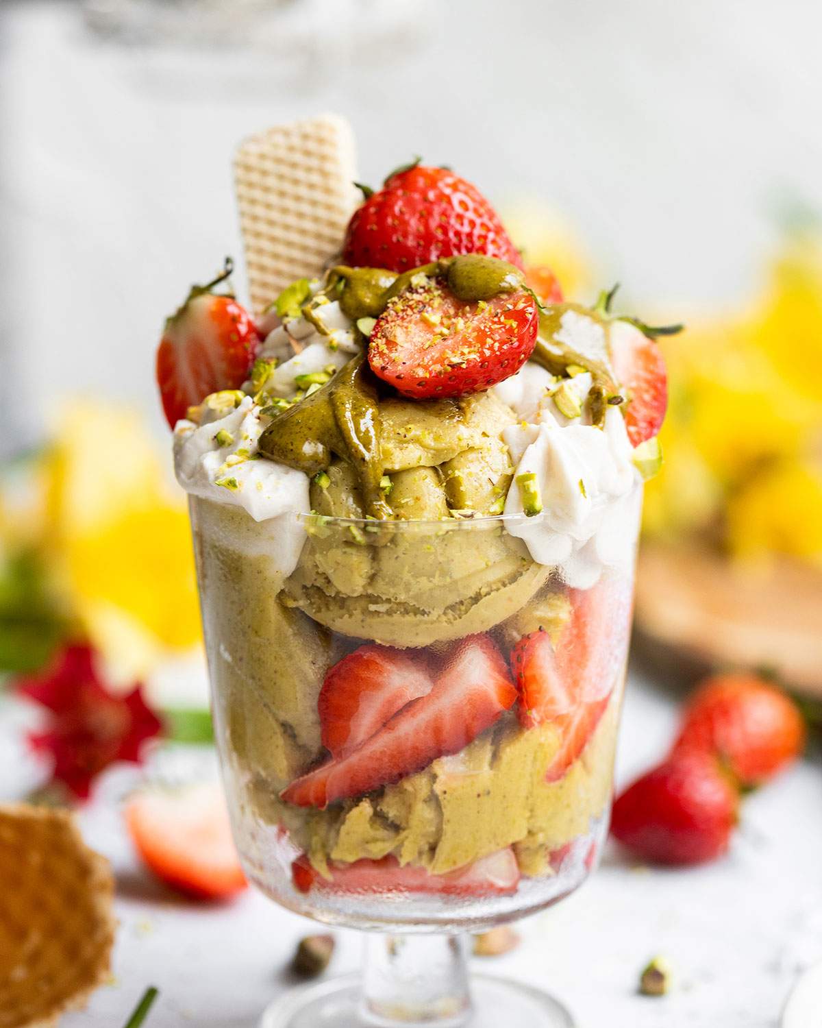 A glass of vegan pistachio ice cream with strawberries, vegan whipped cream and pistachio butter on top.