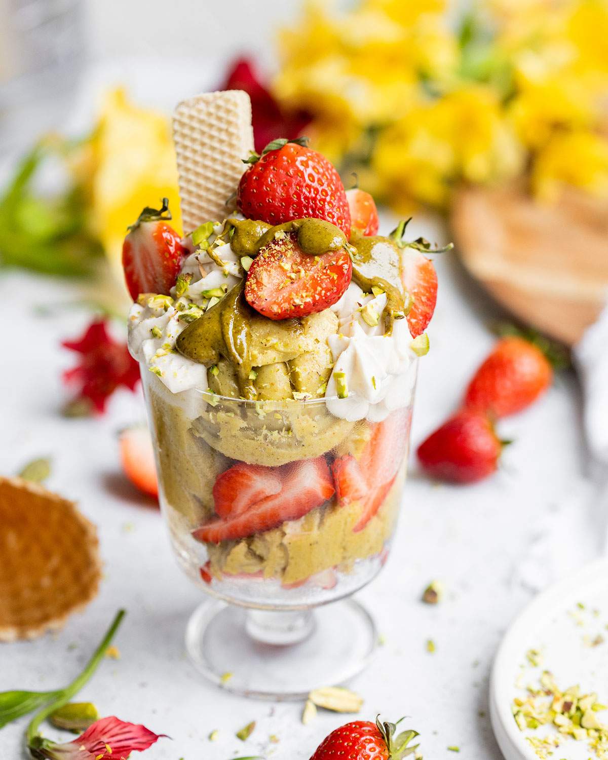 A jar of pistachio ice cream, decorated with fresh strawberries, whipped cream and smooth pistachio butter.