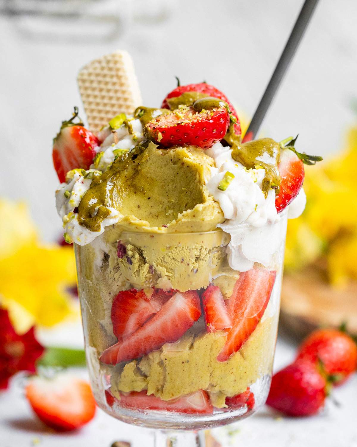 Vegan pistachio ice cream in a glass jar with fresh strawberries, whipped oat cream, smooth pistachio butter and a wafer on the side.