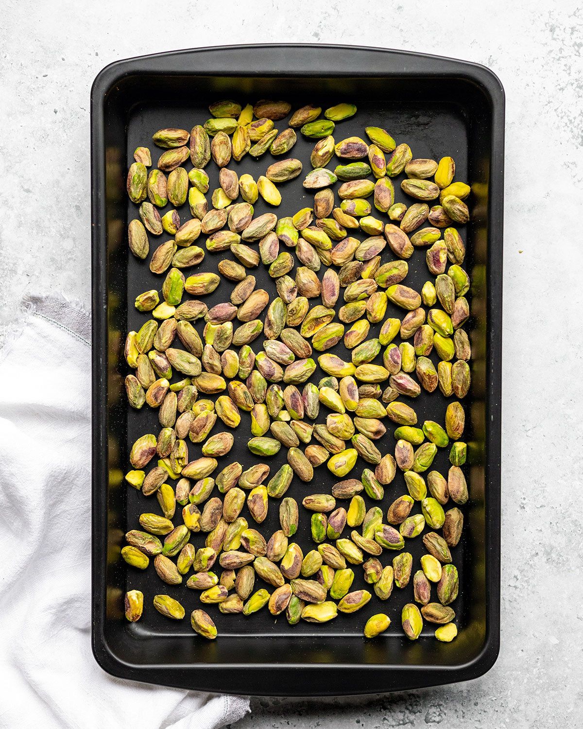 Green pistachio nuts on an oven tray.