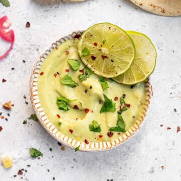 Vegan Avocado lime crema in a bowl with two slices of lime on the edge.