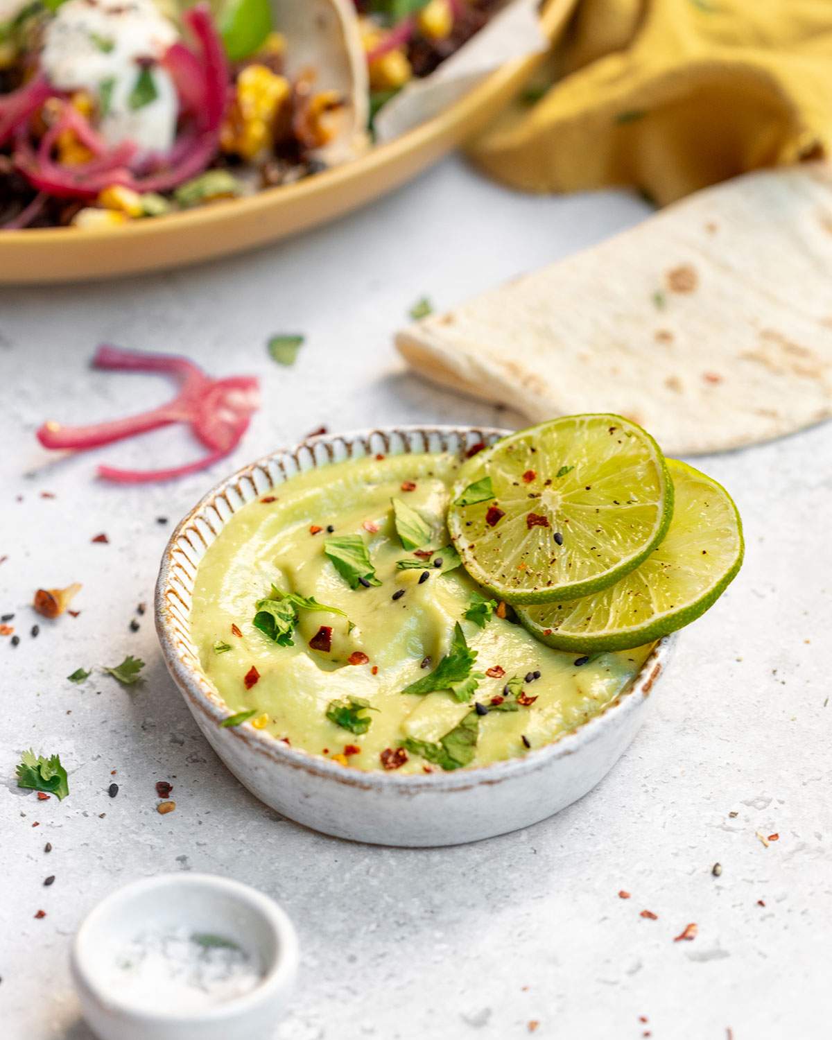 Vegan Avocado lime crema in a bowl with two slices of lime on the edge.