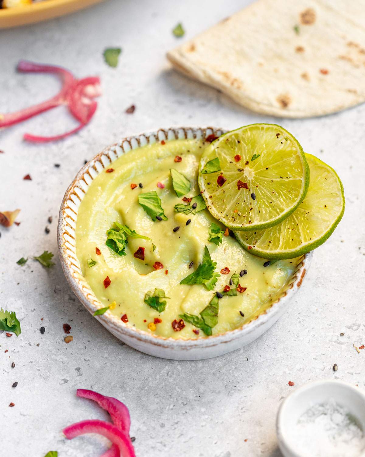 Vegan Avocado lime crema in a bowl with two slices of lime on the edge.